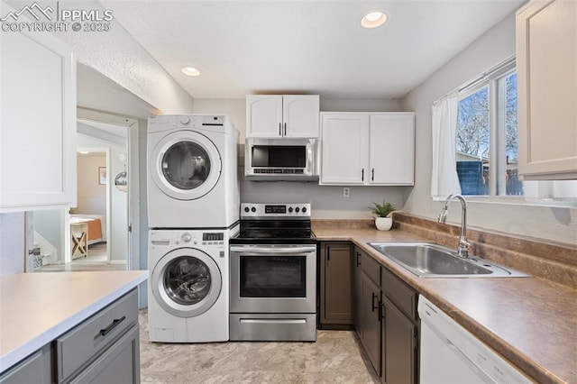 kitchen featuring stacked washer / drying machine, sink, white cabinetry, and appliances with stainless steel finishes