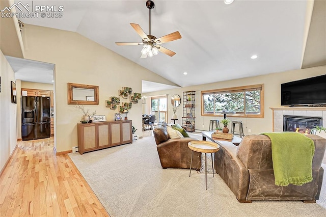 living room with a baseboard radiator, lofted ceiling, light hardwood / wood-style flooring, ceiling fan, and a tile fireplace