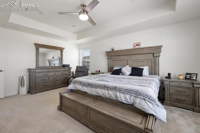 bedroom featuring a tray ceiling, light colored carpet, ceiling fan, and visible vents