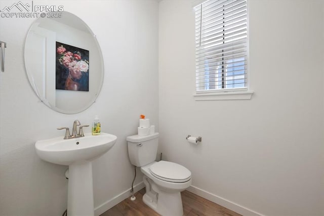 half bathroom featuring a sink, wood finished floors, toilet, and baseboards