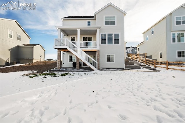 snow covered back of property featuring stairs and fence