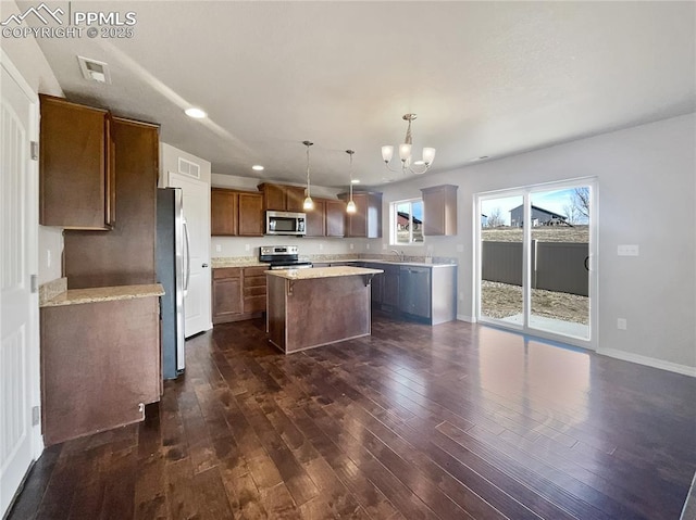 kitchen with appliances with stainless steel finishes, a center island, dark hardwood / wood-style flooring, pendant lighting, and sink