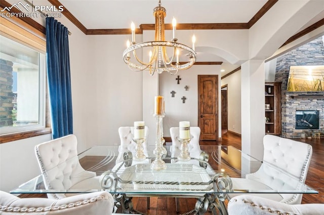 dining area featuring dark wood-type flooring, crown molding, a notable chandelier, and a fireplace