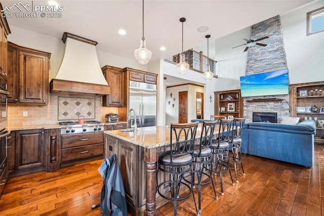 kitchen featuring backsplash, premium range hood, a center island with sink, a kitchen bar, and stainless steel appliances