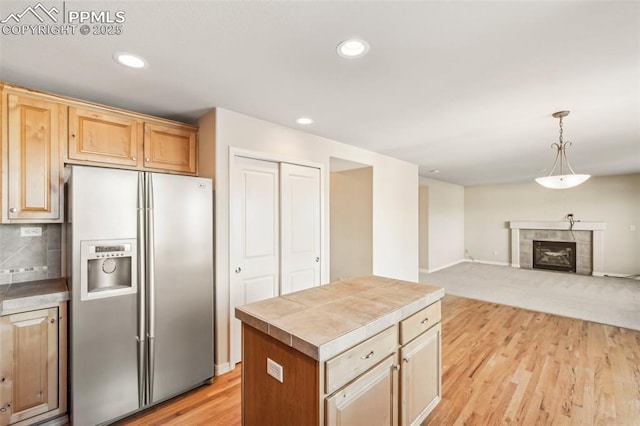 kitchen with decorative light fixtures, tasteful backsplash, a tile fireplace, a kitchen island, and stainless steel fridge with ice dispenser