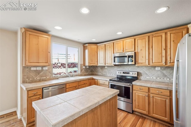 kitchen featuring light hardwood / wood-style floors, appliances with stainless steel finishes, tile counters, sink, and a center island