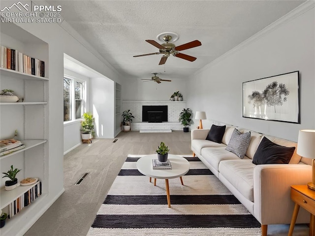 living room with a textured ceiling, ceiling fan, ornamental molding, a brick fireplace, and light colored carpet