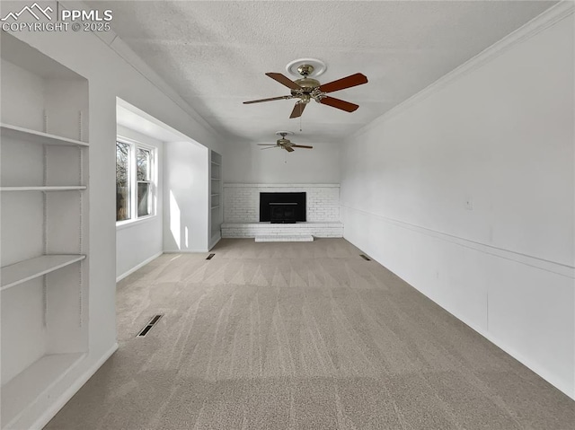 unfurnished living room featuring light carpet, a brick fireplace, ceiling fan, a textured ceiling, and crown molding