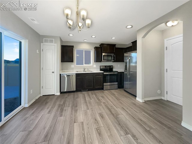 kitchen with dark brown cabinetry, stainless steel appliances, an inviting chandelier, light hardwood / wood-style floors, and sink