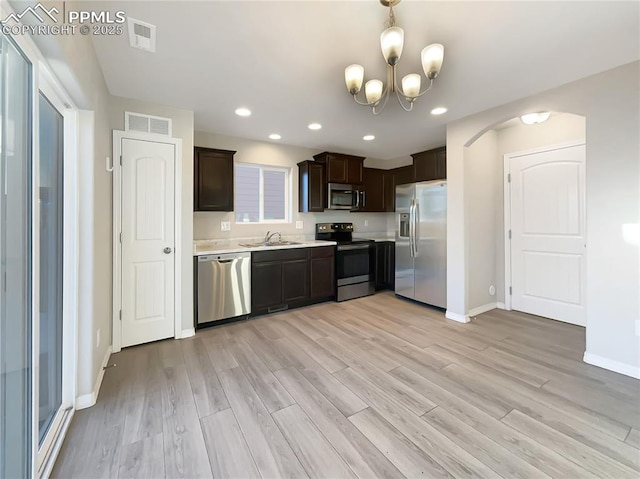 kitchen featuring dark brown cabinets, appliances with stainless steel finishes, sink, light hardwood / wood-style floors, and an inviting chandelier