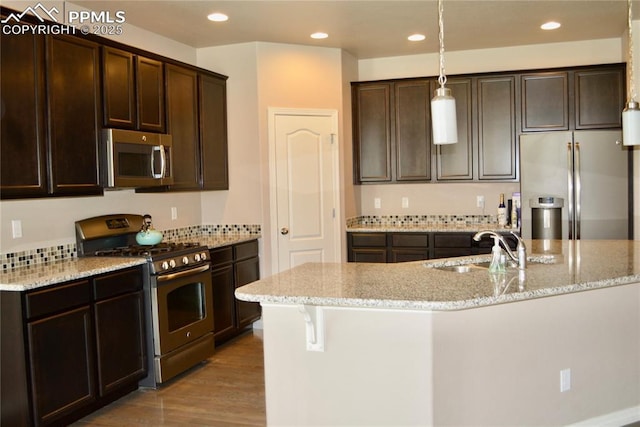 kitchen featuring sink, decorative light fixtures, appliances with stainless steel finishes, an island with sink, and light hardwood / wood-style floors