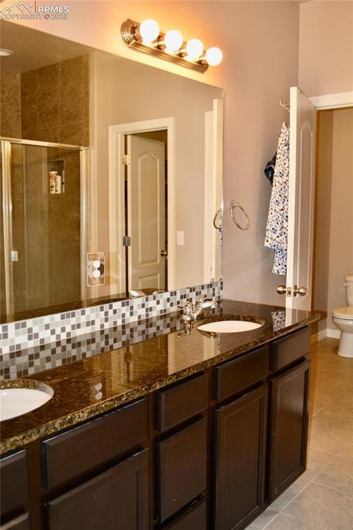 bathroom with tile patterned flooring, tasteful backsplash, vanity, toilet, and walk in shower