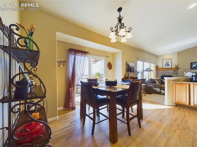 dining space featuring light hardwood / wood-style floors, a chandelier, lofted ceiling, and a stone fireplace