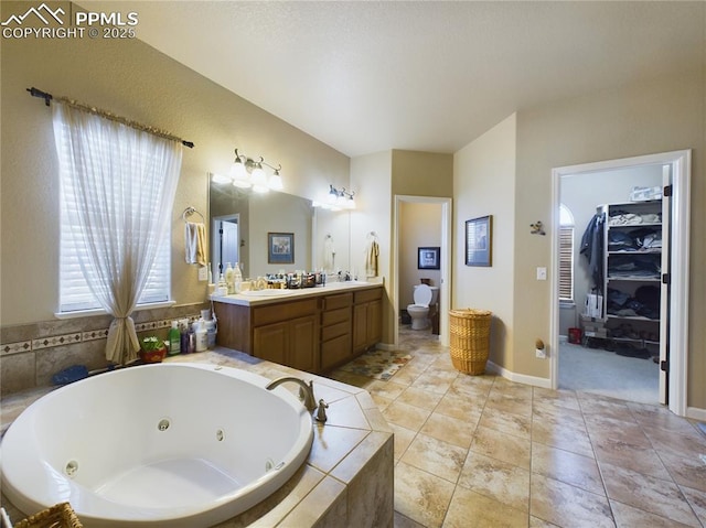 bathroom with toilet, tile patterned flooring, a relaxing tiled tub, and vanity