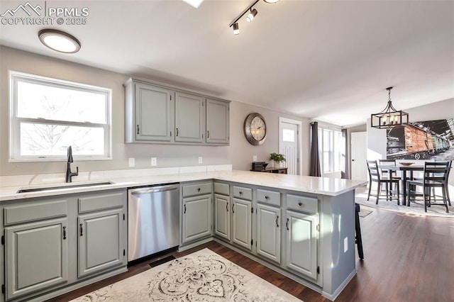 kitchen featuring gray cabinetry, a peninsula, a sink, stainless steel dishwasher, and dark wood-style floors