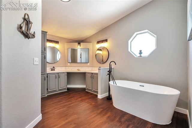 bathroom with vaulted ceiling, a bathtub, hardwood / wood-style flooring, and vanity