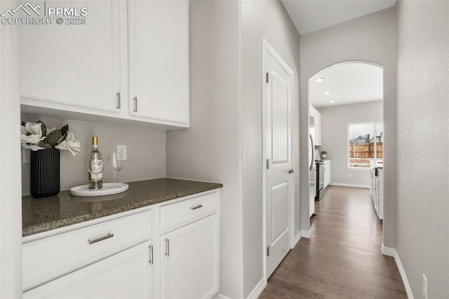 bar with dark stone countertops, white cabinetry, and dark hardwood / wood-style flooring