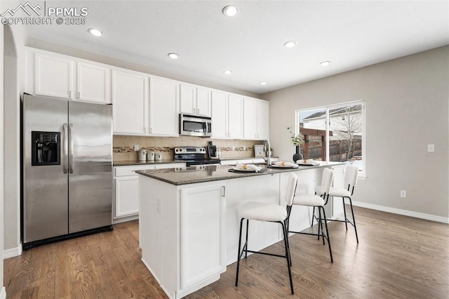 kitchen with hardwood / wood-style flooring, white cabinets, stainless steel appliances, and an island with sink