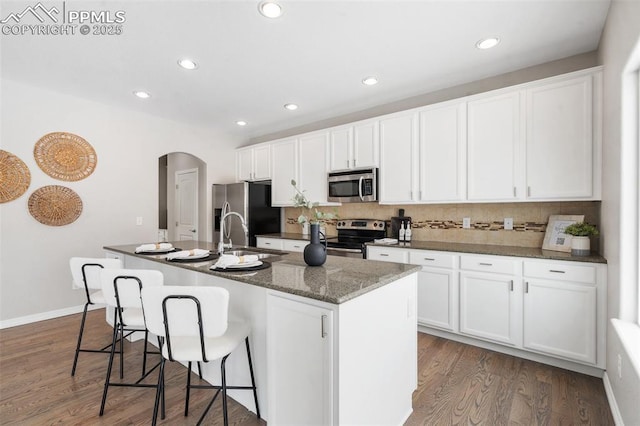 kitchen featuring white cabinets, sink, dark wood-type flooring, stainless steel appliances, and a center island with sink