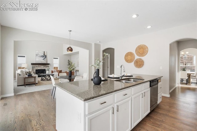 kitchen featuring dishwasher, sink, white cabinetry, dark stone counters, and an island with sink