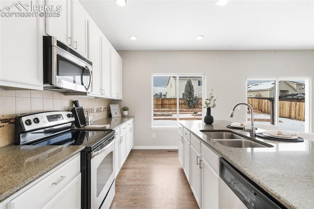 kitchen with light hardwood / wood-style flooring, appliances with stainless steel finishes, sink, white cabinetry, and light stone counters