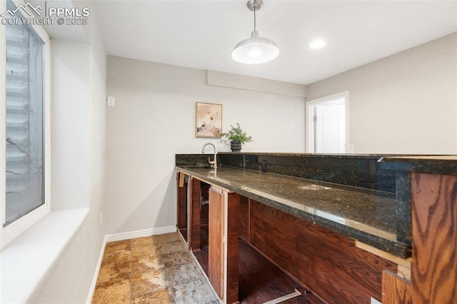 bar featuring sink, decorative light fixtures, and dark stone counters