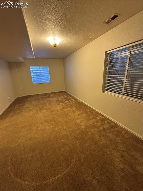 carpeted empty room featuring a textured ceiling, visible vents, and baseboards