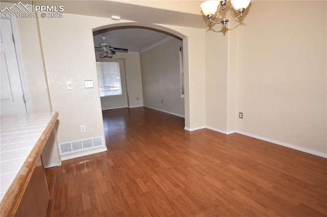 unfurnished dining area featuring arched walkways, ceiling fan with notable chandelier, dark wood-type flooring, visible vents, and baseboards