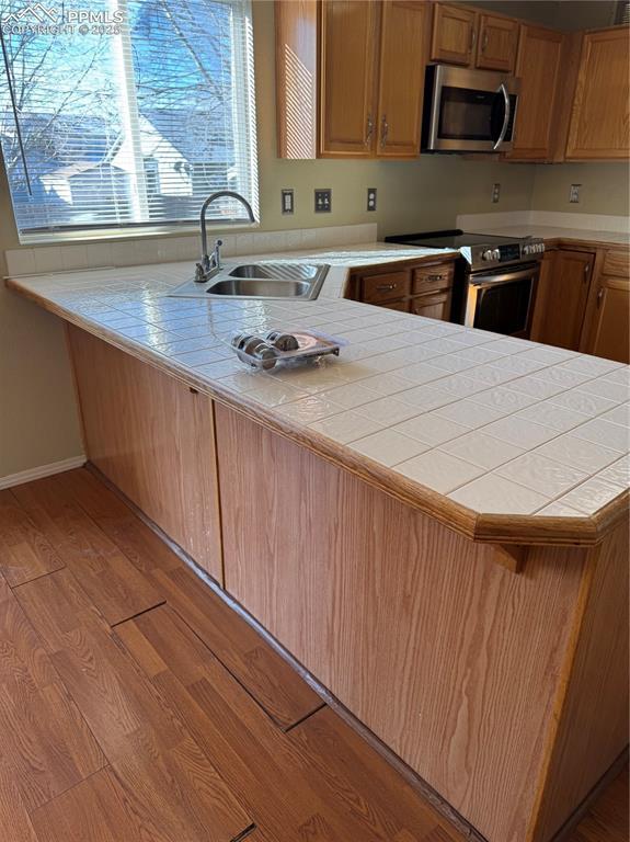 kitchen with appliances with stainless steel finishes, tile countertops, sink, kitchen peninsula, and light wood-type flooring