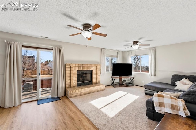 living room with a textured ceiling, a brick fireplace, hardwood / wood-style floors, and ceiling fan