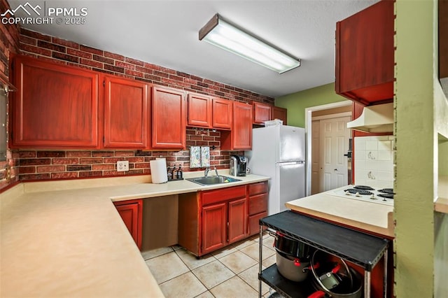 kitchen featuring premium range hood, sink, white appliances, light tile patterned floors, and brick wall