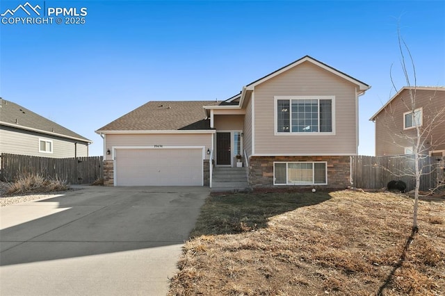 tri-level home with driveway, stone siding, an attached garage, and fence