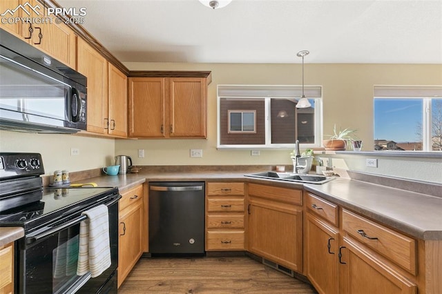 kitchen with visible vents, hanging light fixtures, a sink, wood finished floors, and black appliances