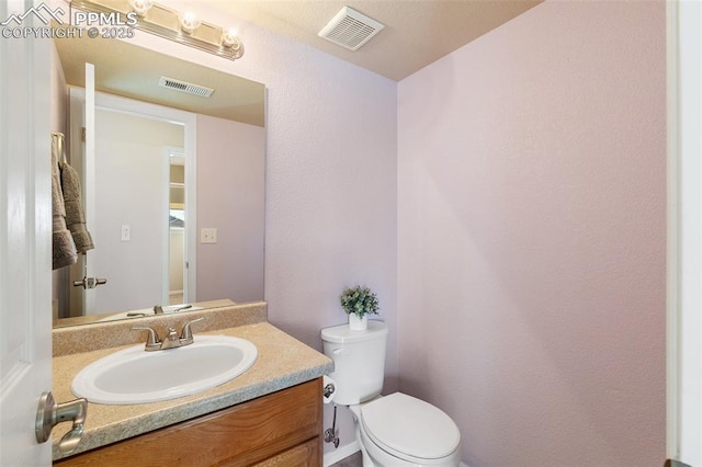 bathroom with toilet, vanity, and visible vents