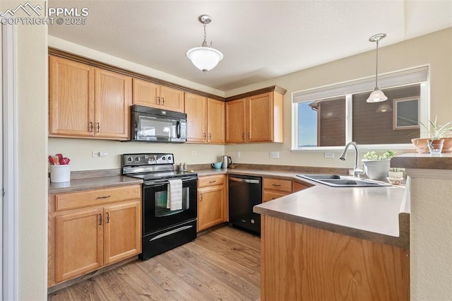 kitchen featuring black appliances, light wood-style flooring, pendant lighting, and a sink