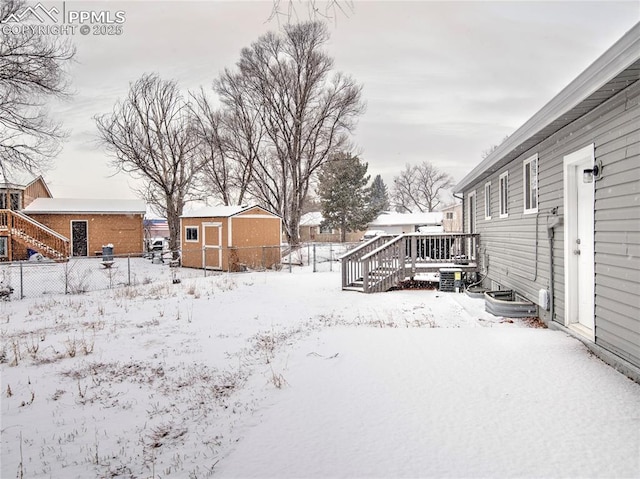 yard covered in snow with a wooden deck and a shed