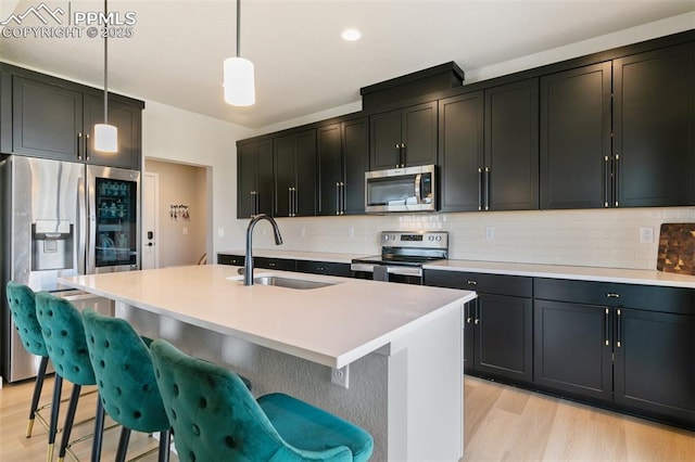 kitchen featuring appliances with stainless steel finishes, pendant lighting, an island with sink, and sink