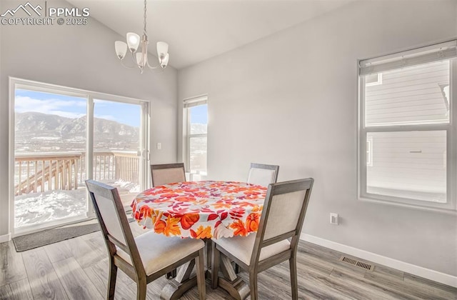 dining space with wood-type flooring, a mountain view, vaulted ceiling, and a notable chandelier