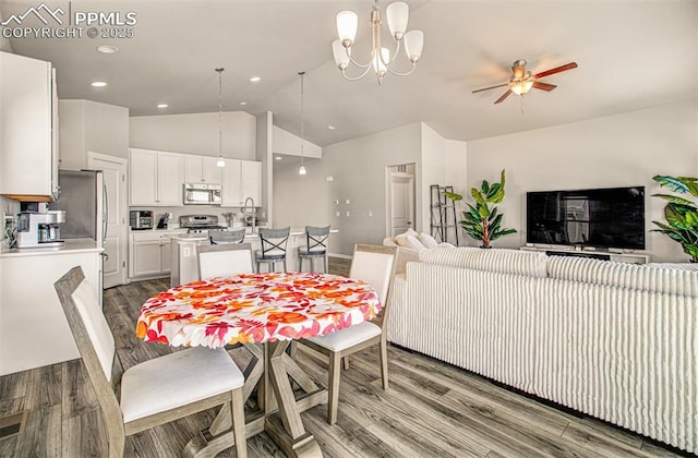 dining room featuring ceiling fan with notable chandelier, wood-type flooring, sink, and vaulted ceiling