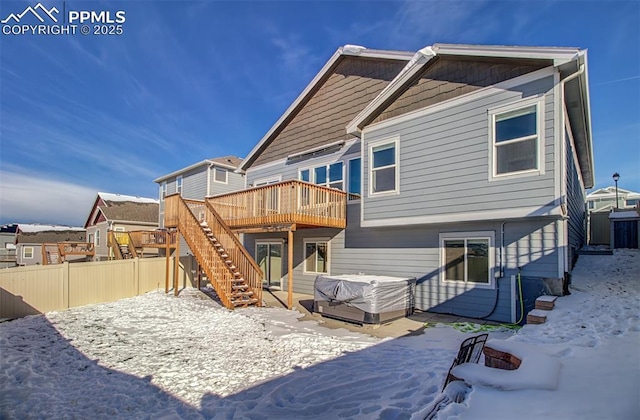 snow covered rear of property featuring a wooden deck and a jacuzzi