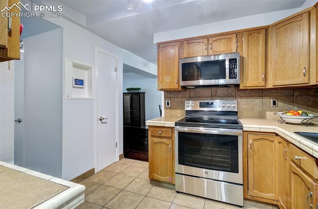 kitchen with tile countertops, light tile patterned flooring, tasteful backsplash, and stainless steel appliances