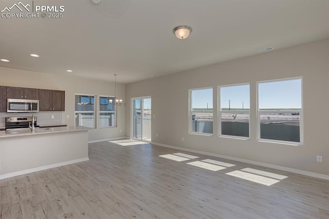 interior space with decorative light fixtures, stainless steel appliances, sink, light wood-type flooring, and dark brown cabinets