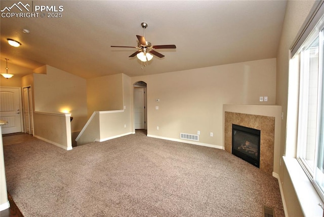 unfurnished living room featuring ceiling fan, a healthy amount of sunlight, a tile fireplace, and carpet