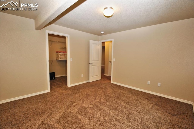 unfurnished bedroom featuring beam ceiling, a textured ceiling, dark carpet, a walk in closet, and a closet