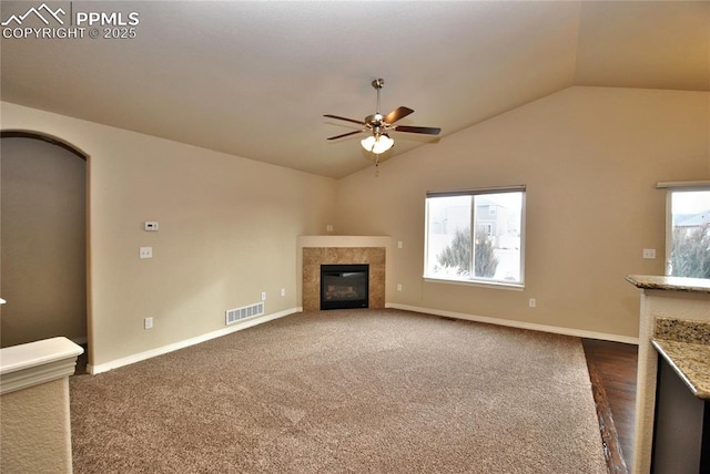 unfurnished living room with vaulted ceiling, a tile fireplace, ceiling fan, and dark colored carpet