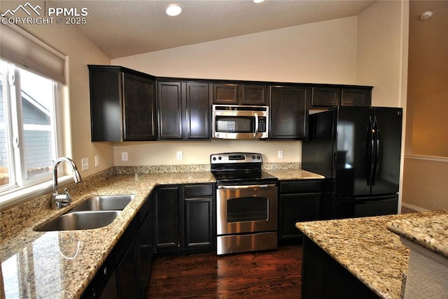 kitchen with stainless steel appliances, vaulted ceiling, light stone countertops, and sink