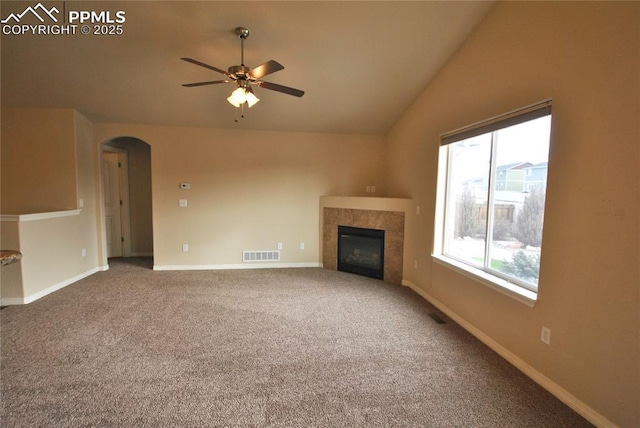 unfurnished living room featuring a tiled fireplace, vaulted ceiling, carpet floors, and ceiling fan