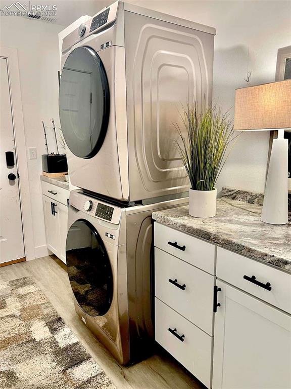 laundry area featuring light wood-type flooring, cabinets, and stacked washer / drying machine