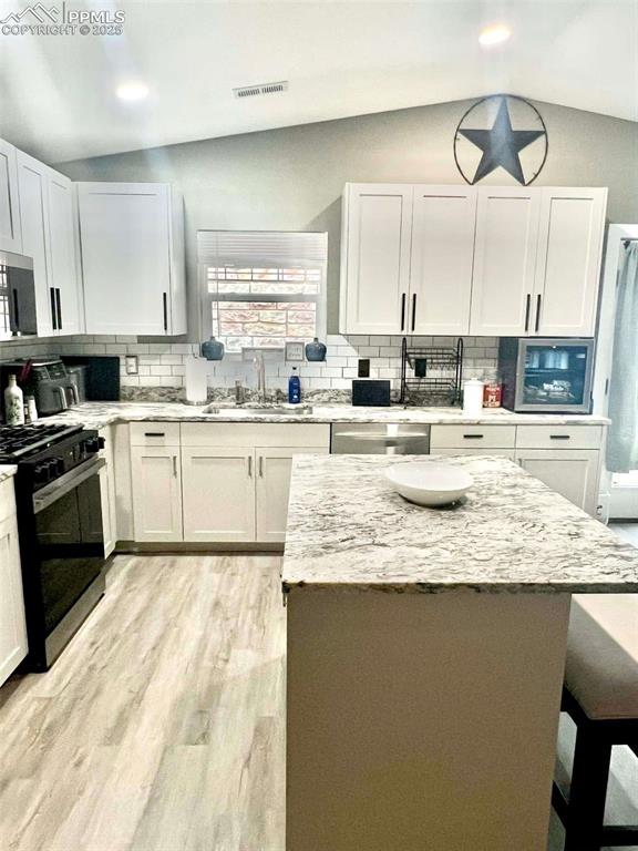 kitchen featuring appliances with stainless steel finishes, light stone countertops, vaulted ceiling, white cabinets, and sink