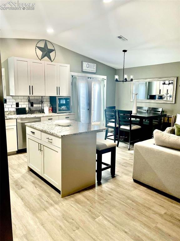 kitchen featuring white cabinets, vaulted ceiling, a center island, and pendant lighting